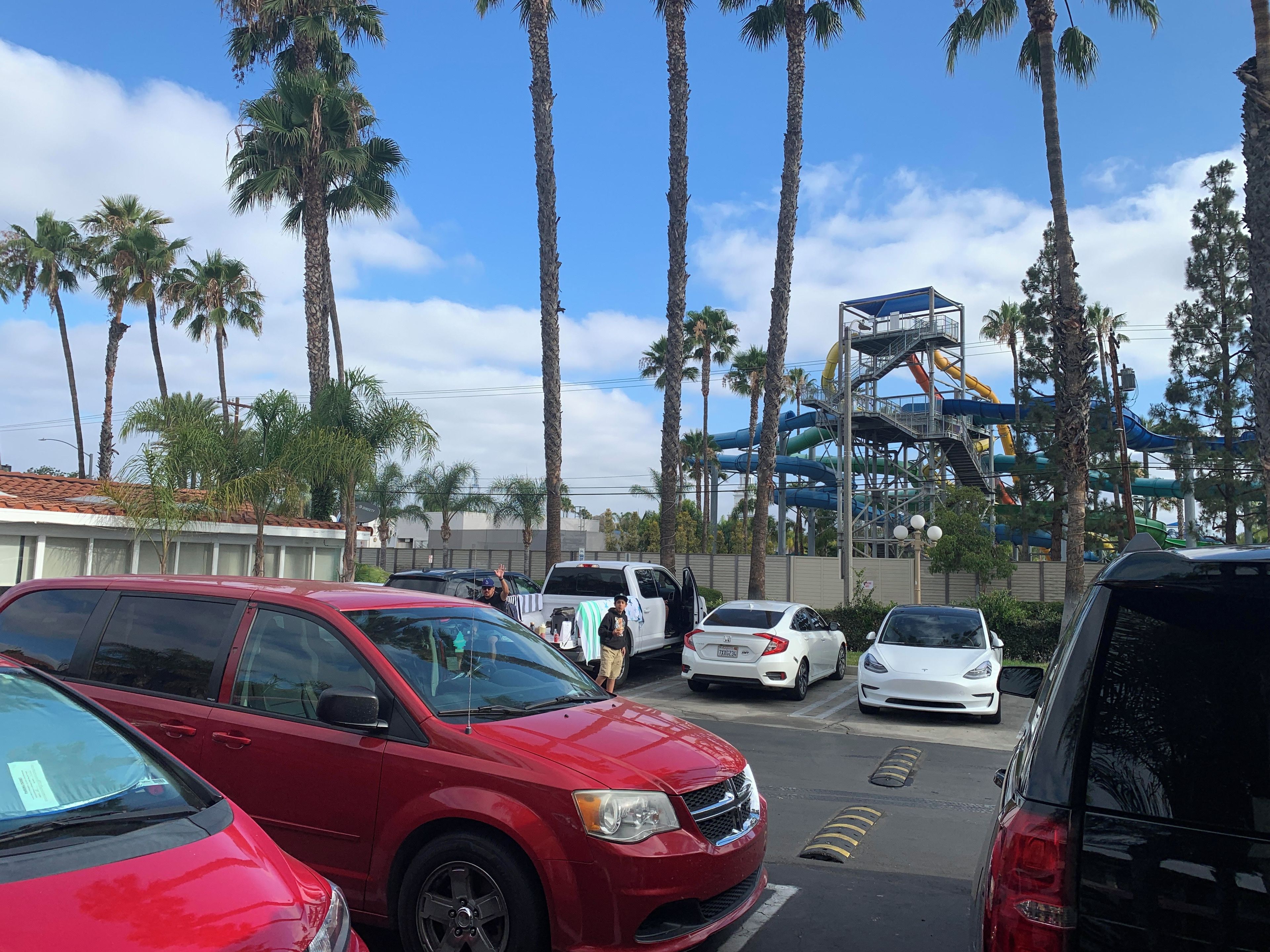 A parking lot with several cars, palm trees, and a water park in the background.