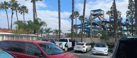 A parking lot with several cars, palm trees, and a water park in the background.