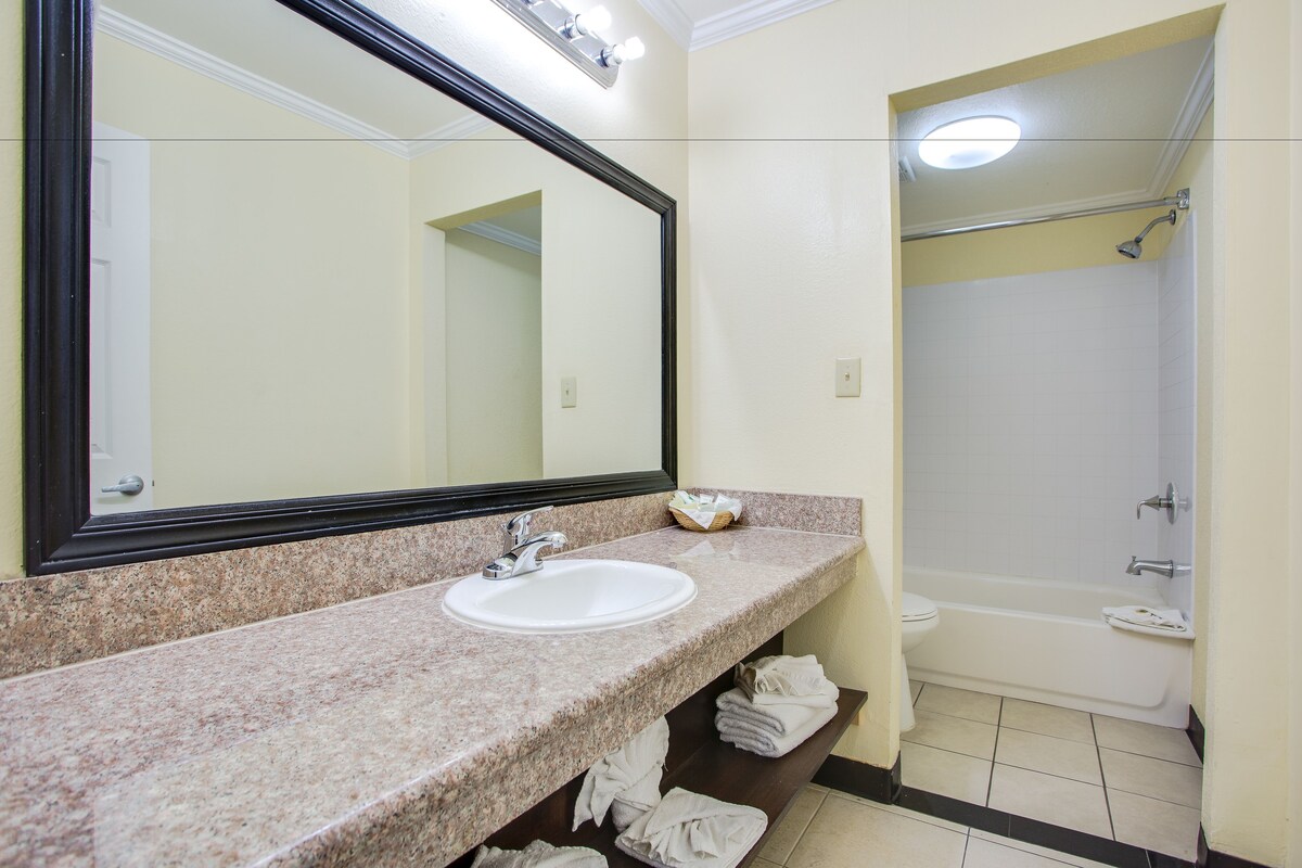A bathroom with a granite countertop sink, a large mirror, and a white bathtub.