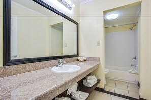 A bathroom with a granite countertop sink, a large mirror, and a white bathtub. - Best Inn & Suites (Buena Park)