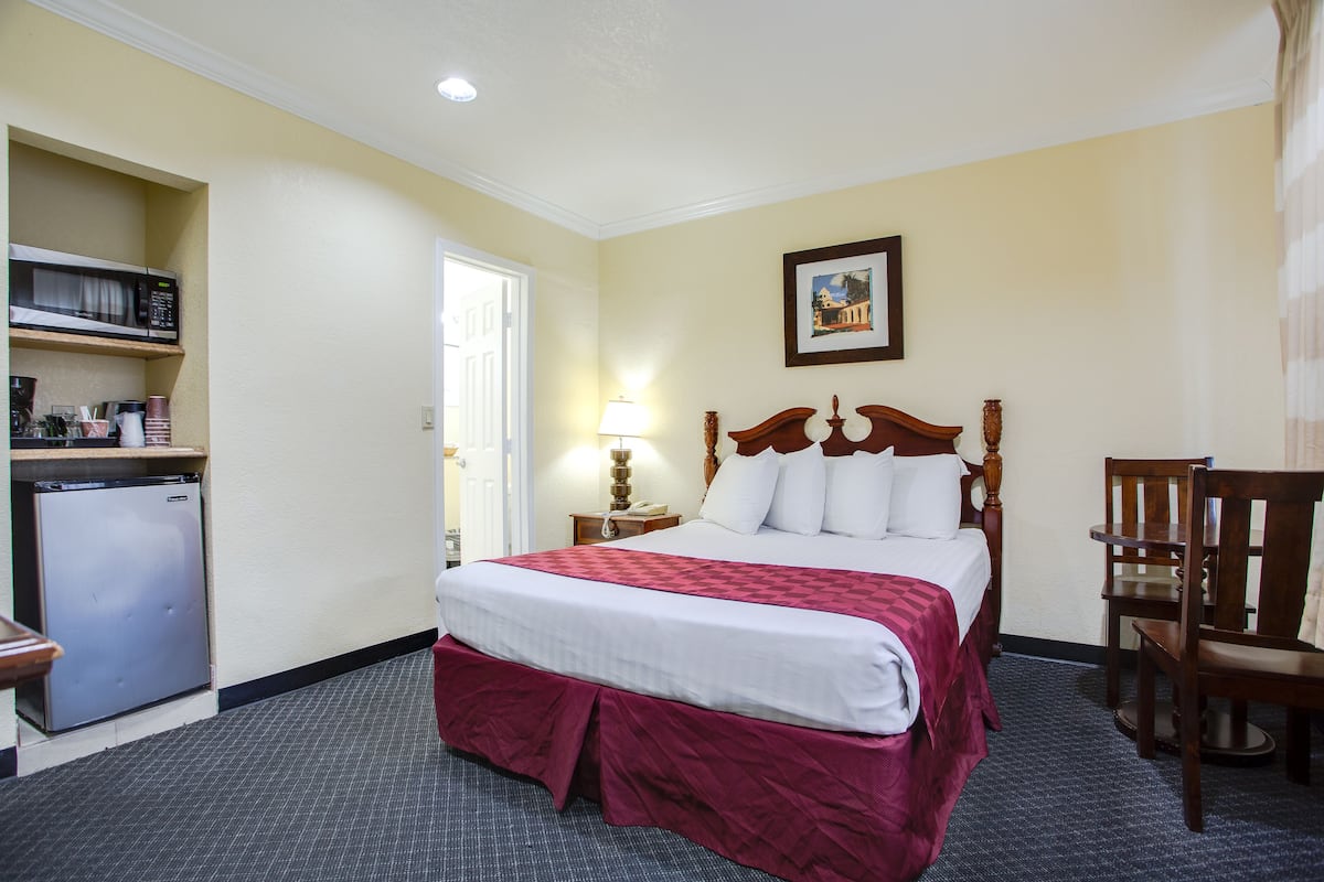 A hotel room with a bed, a desk, a chair, a microwave, and a refrigerator.