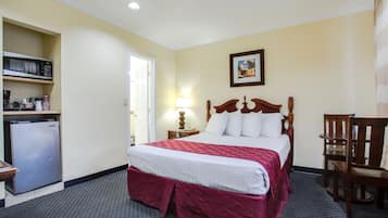 A hotel room with a bed, a desk, a chair, a microwave, and a refrigerator.