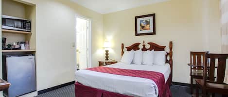 Habitación de hotel con cama, escritorio, silla, microondas y refrigerador.