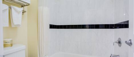 Un baño con una bañera blanca, un inodoro y un perchero con toallas dobladas.