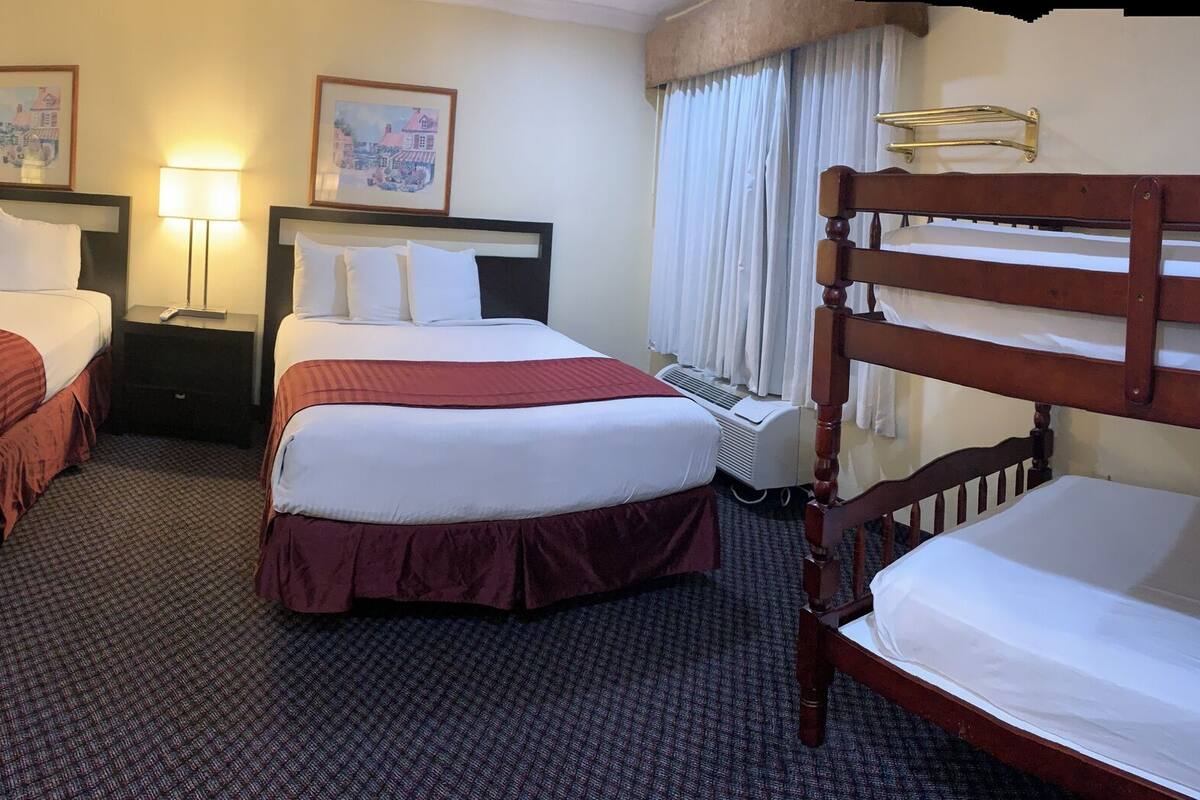 A hotel room with two single beds, a desk with a chair, a large mirror, and a bathroom with a bathtub and shower.