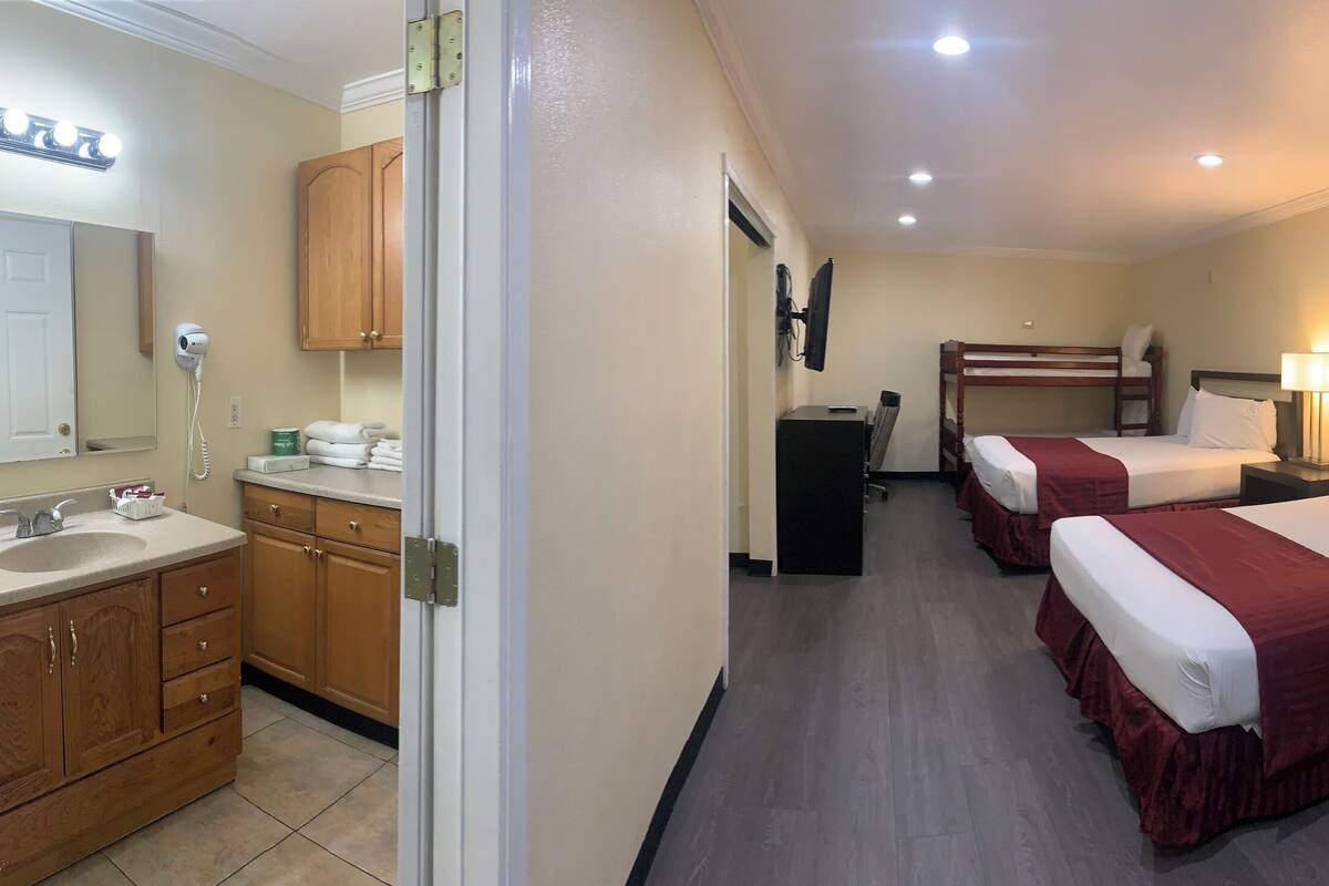 A hotel room with two beds, a bathroom with a sink and mirror, a small kitchenette, and a TV.