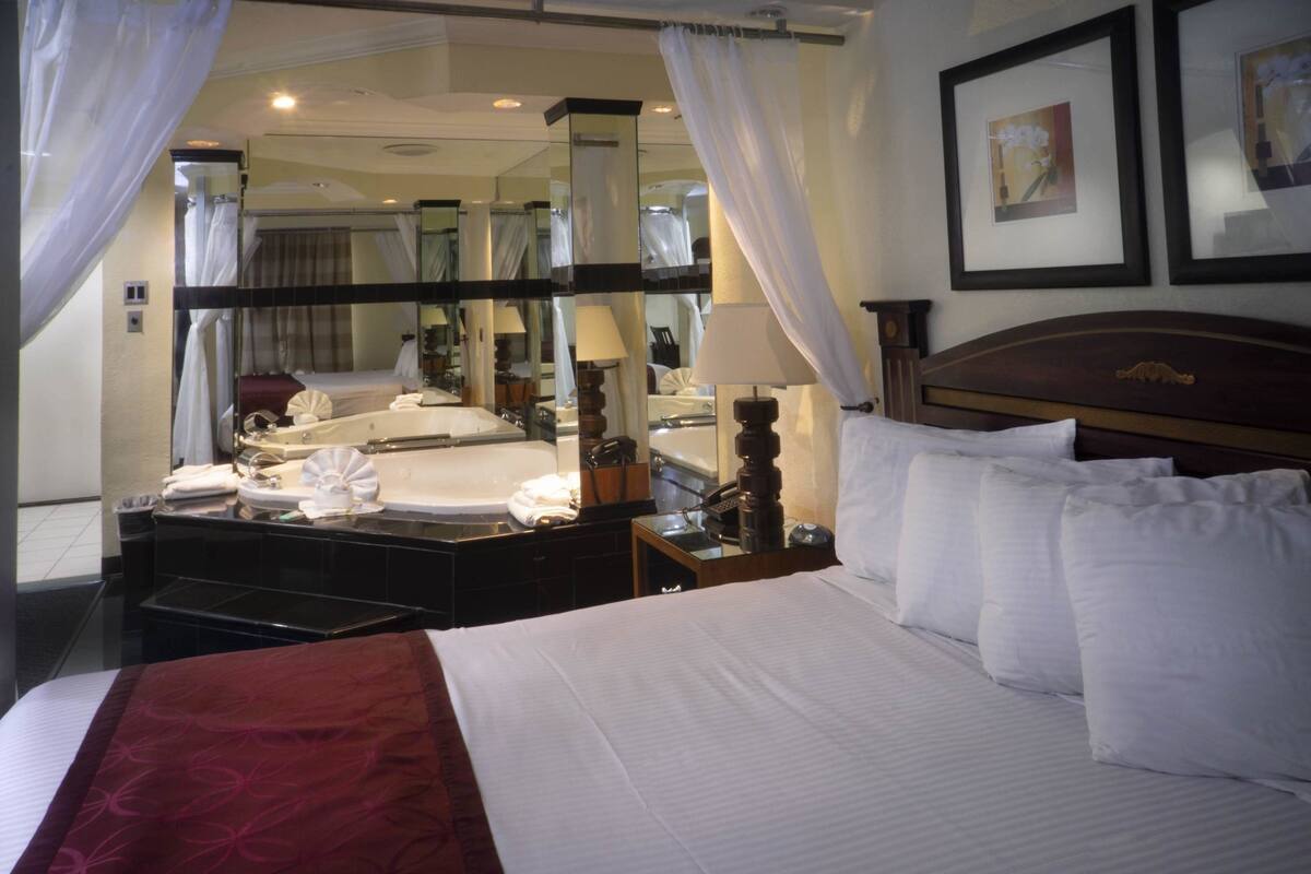 A hotel room with a large bed, a vanity with a mirror, a nightstand, and a bedside table.