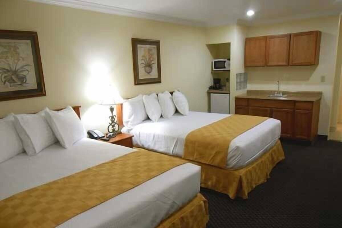 A hotel room with two beds, a small kitchenette, and a framed picture on the wall.