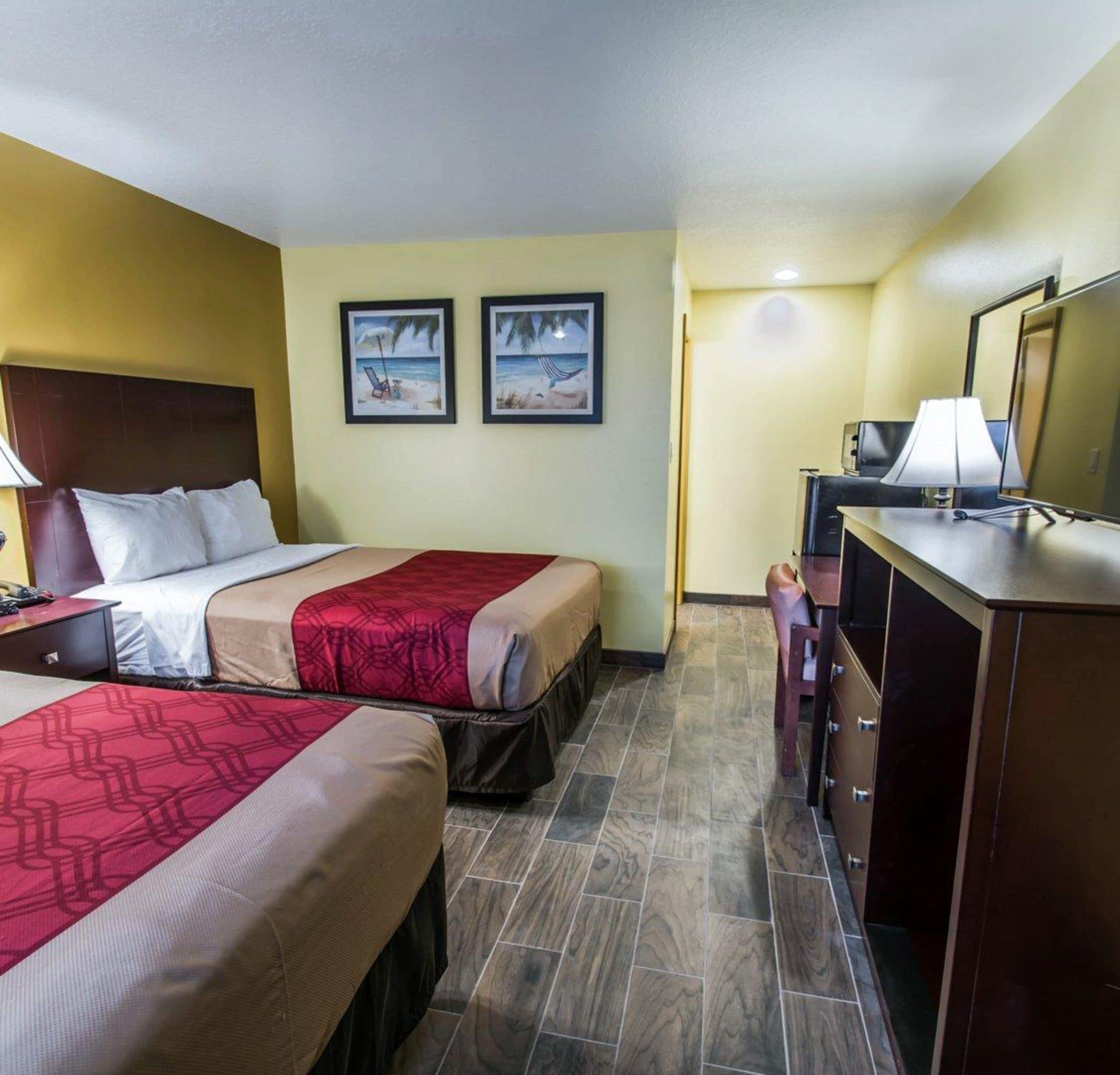 Habitación de hotel con dos camas, un escritorio con lámpara, cómoda y dos cuadros en la pared.