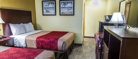 Habitación de hotel con dos camas, un escritorio con lámpara, cómoda y dos cuadros en la pared.