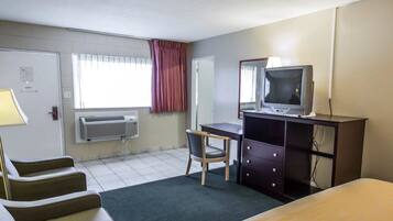 Una habitación de hotel con una cama, un escritorio con computadora, una silla, un televisor y un aire acondicionado.