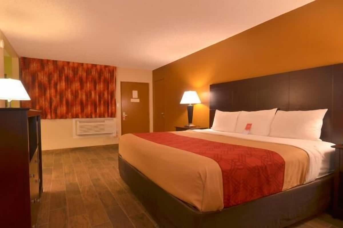 Une chambre d’hôtel avec un lit, deux lampes de chevet, une tête de lit en bois, un mur d’accent rouge et un plancher en bois.