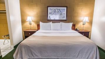 A hotel room with a large bed, two bedside tables with lamps, a framed picture on the wall, and a green carpet.