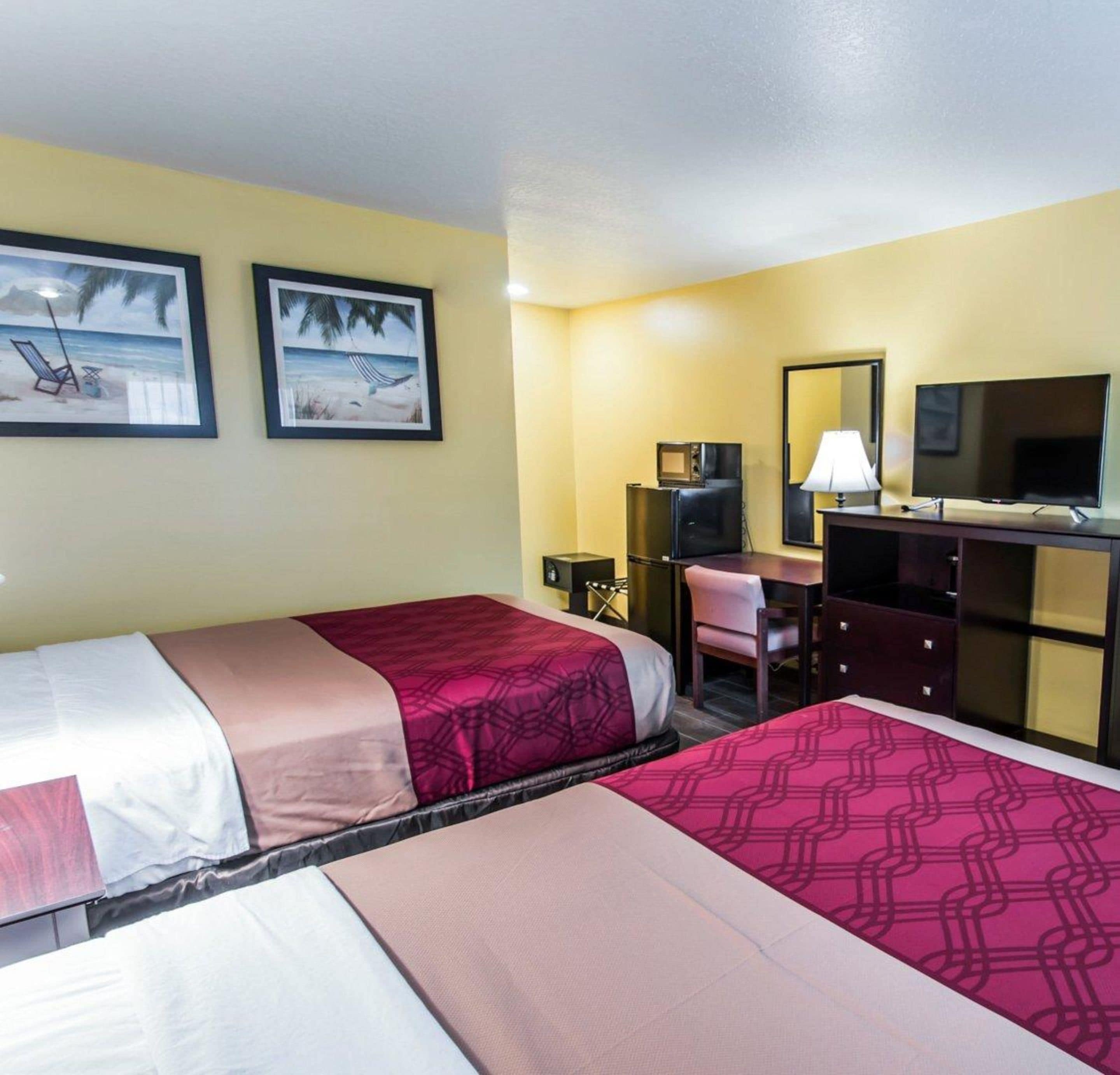 A hotel room with two beds, a desk with a chair, a television, and two framed pictures on the wall.