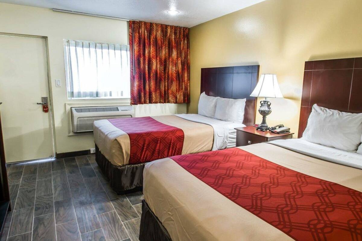 Une chambre d’hôtel avec deux lits, une fenêtre avec des rideaux, un appareil de climatisation et une table de chevet avec une lampe.