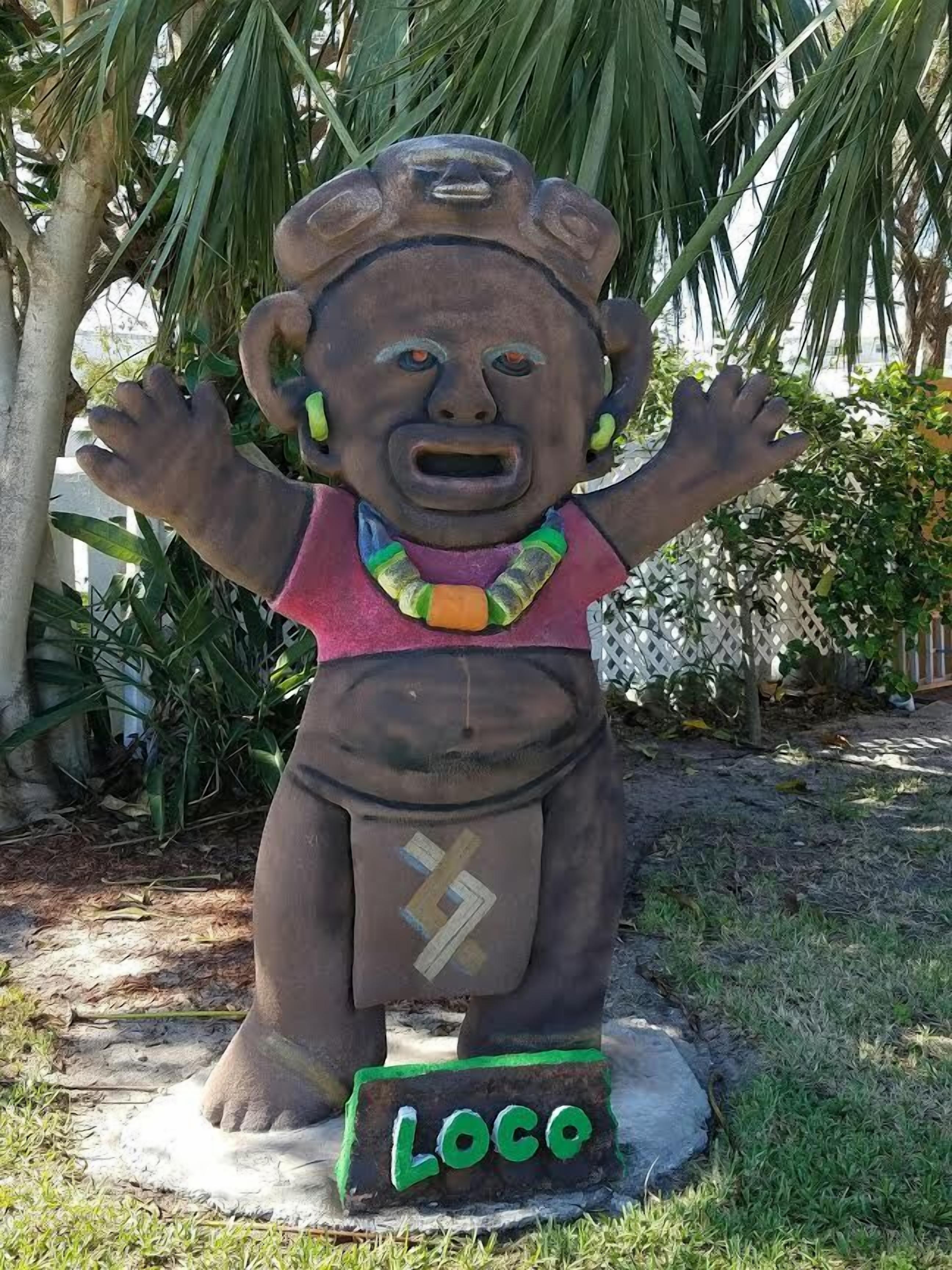 A statue of a figure with outstretched arms, wearing a necklace and a belt with lightning bolt symbols, standing on a base labeled "LOCO."