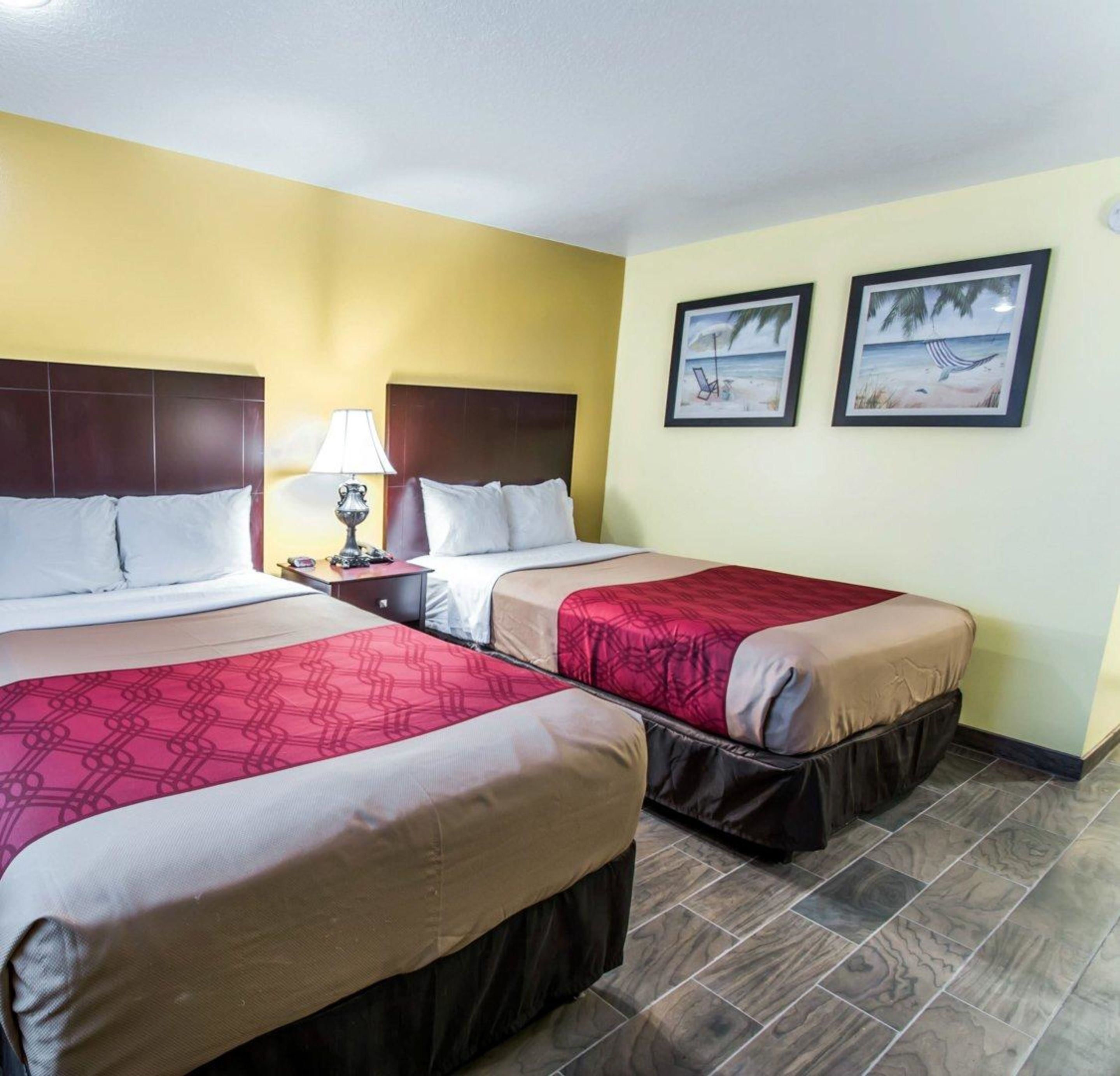 A hotel room with two beds, a nightstand with a lamp, and two framed pictures on the wall.