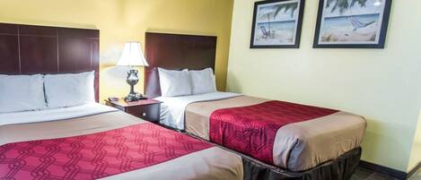 A hotel room with two beds, a nightstand with a lamp, and two framed pictures on the wall.