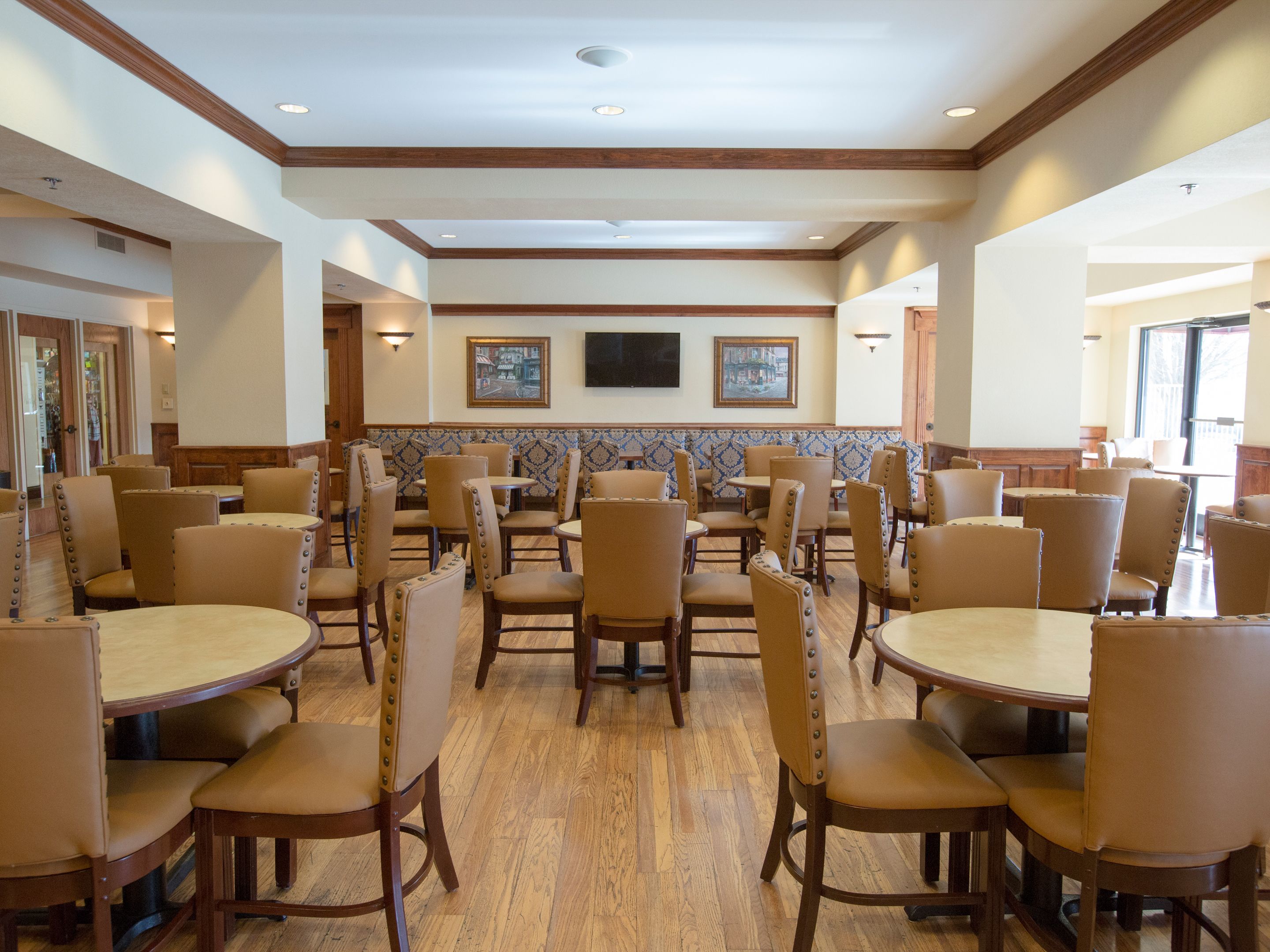 A spacious dining area with multiple tables and chairs, wooden floors, and a tiled backsplash.