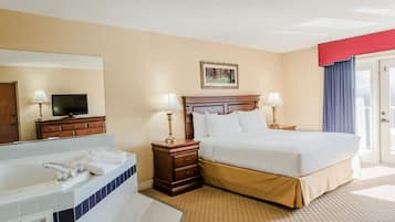 Habitación de hotel con una cama grande, baño con bañera, televisor y un cuadro en la pared.