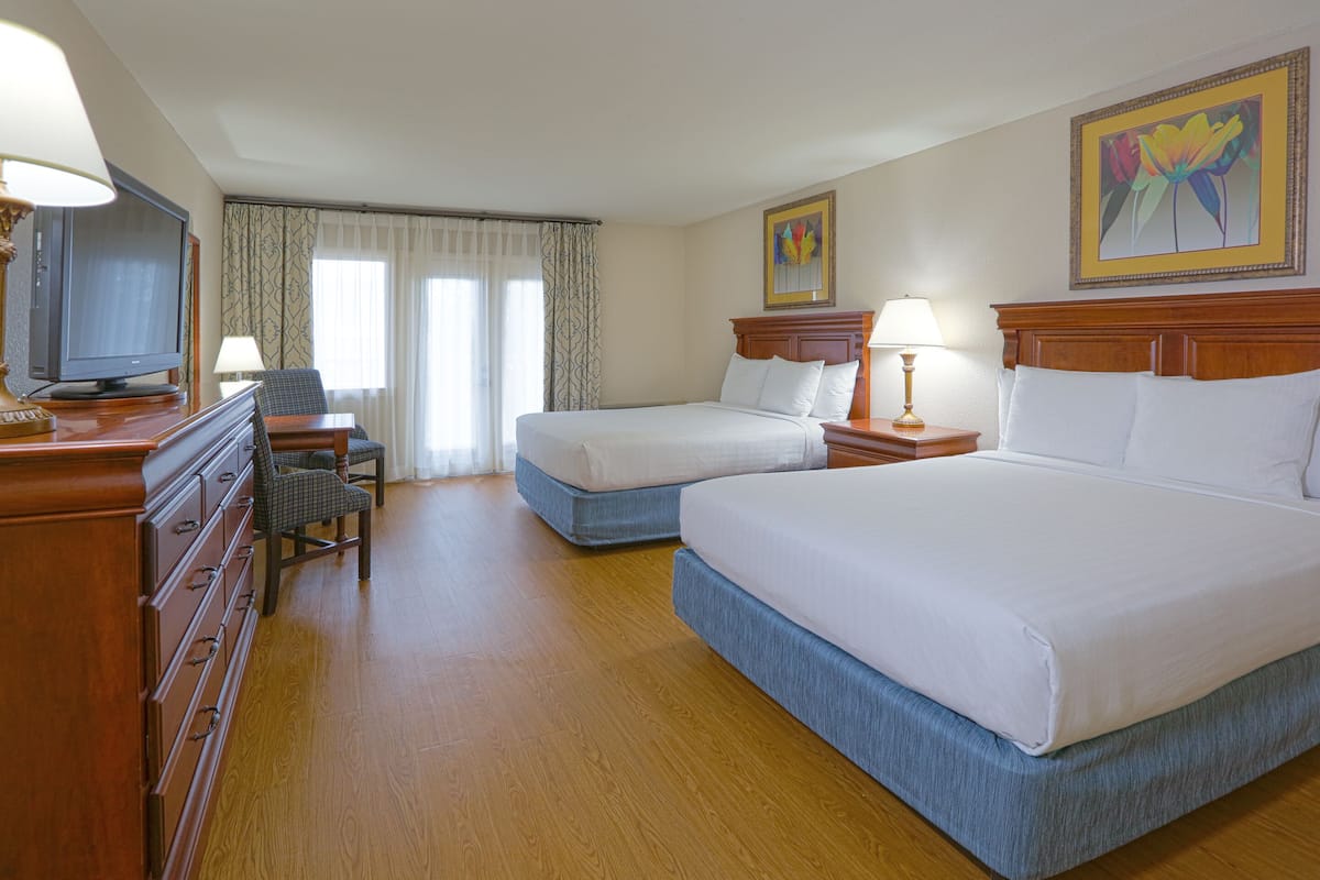 Quarto de hotel com duas camas, uma escrivaninha, uma televisão e uma cadeira.