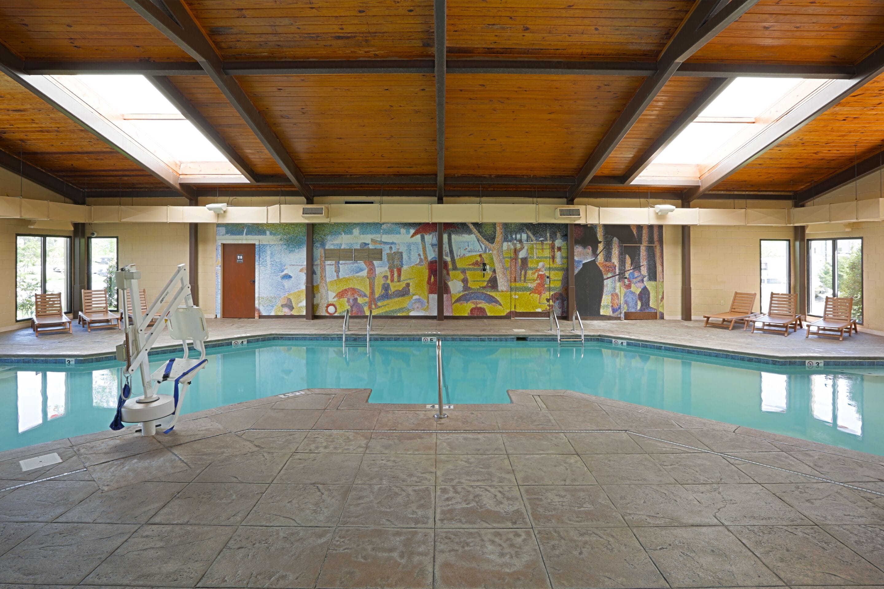 A swimming pool with a wooden ceiling, tiled floor, and a mural on the back wall.
