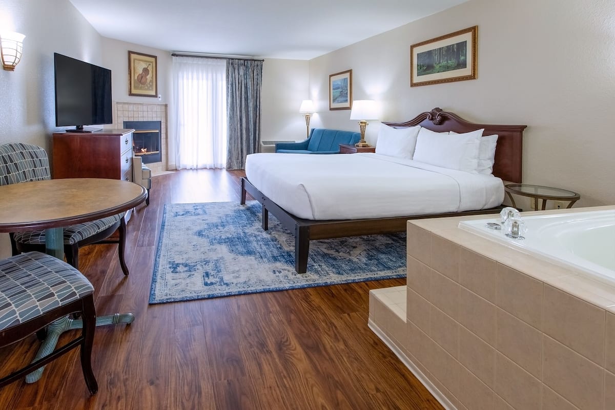 Quarto de hotel com cama, área de estar com mesa e cadeiras, televisão, lareira e banheira.