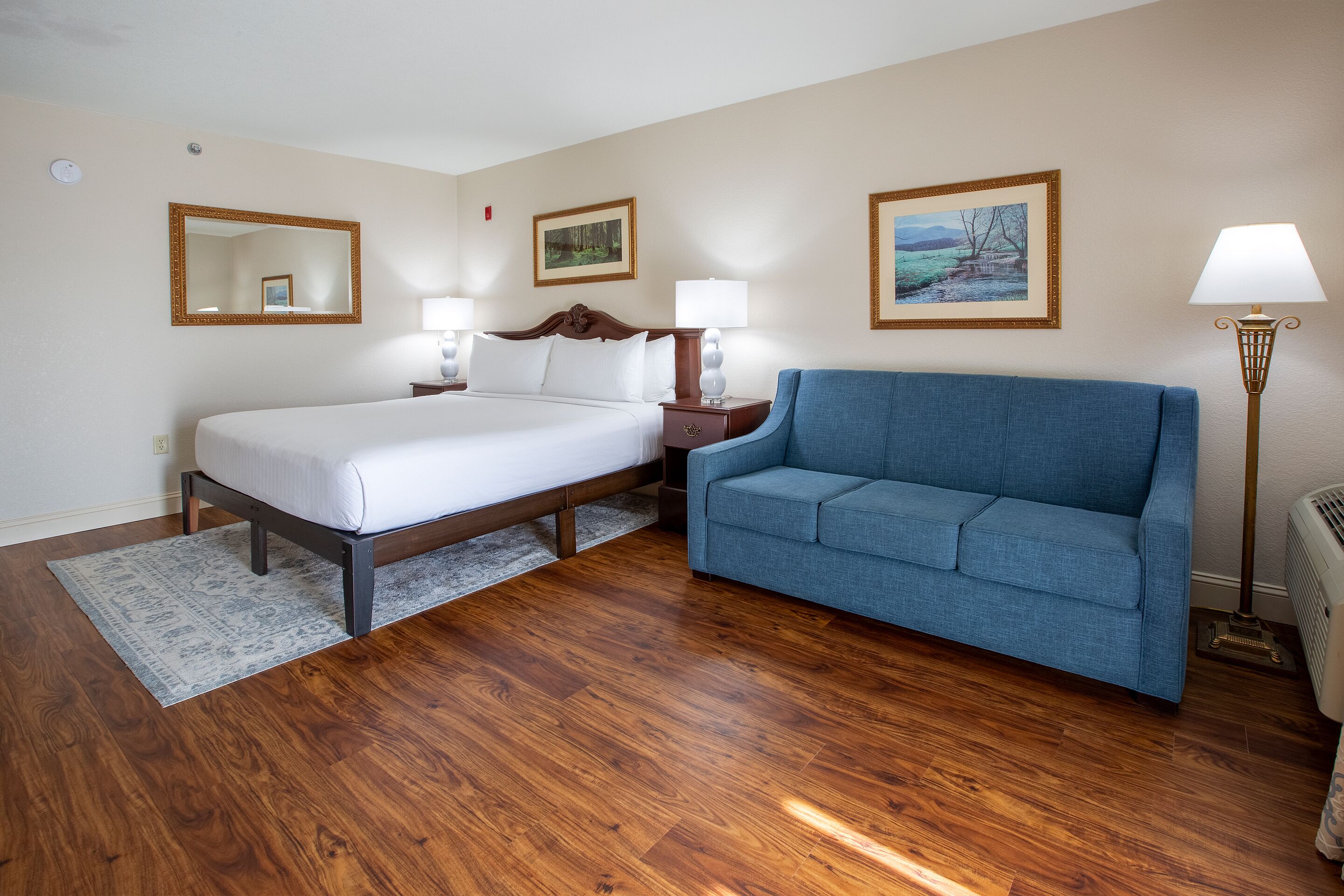 Une chambre d’hôtel avec un lit, un canapé bleu, un plancher en bois et deux lampes fixées au mur.