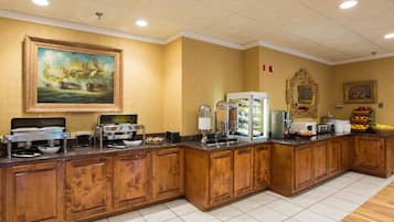 Un long comptoir de buffet avec différents postes de service pour la nourriture, un tableau au mur et un miroir.