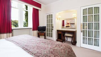 Habitación de hotel con cama, escritorio, televisor, espejo y vista a zonas verdes.