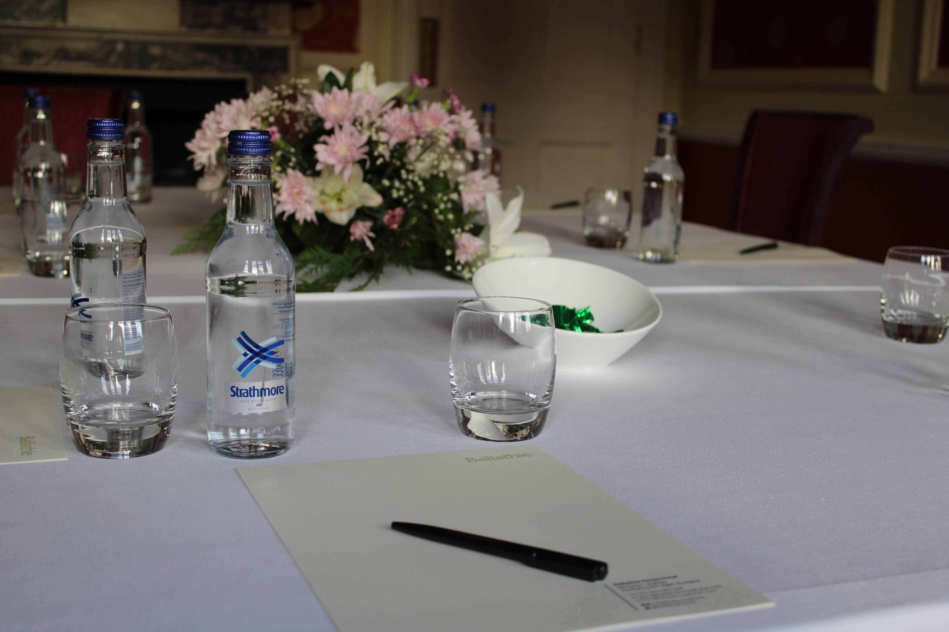 A table set with clear glasses, a bottle of water, a pen, and a bowl.