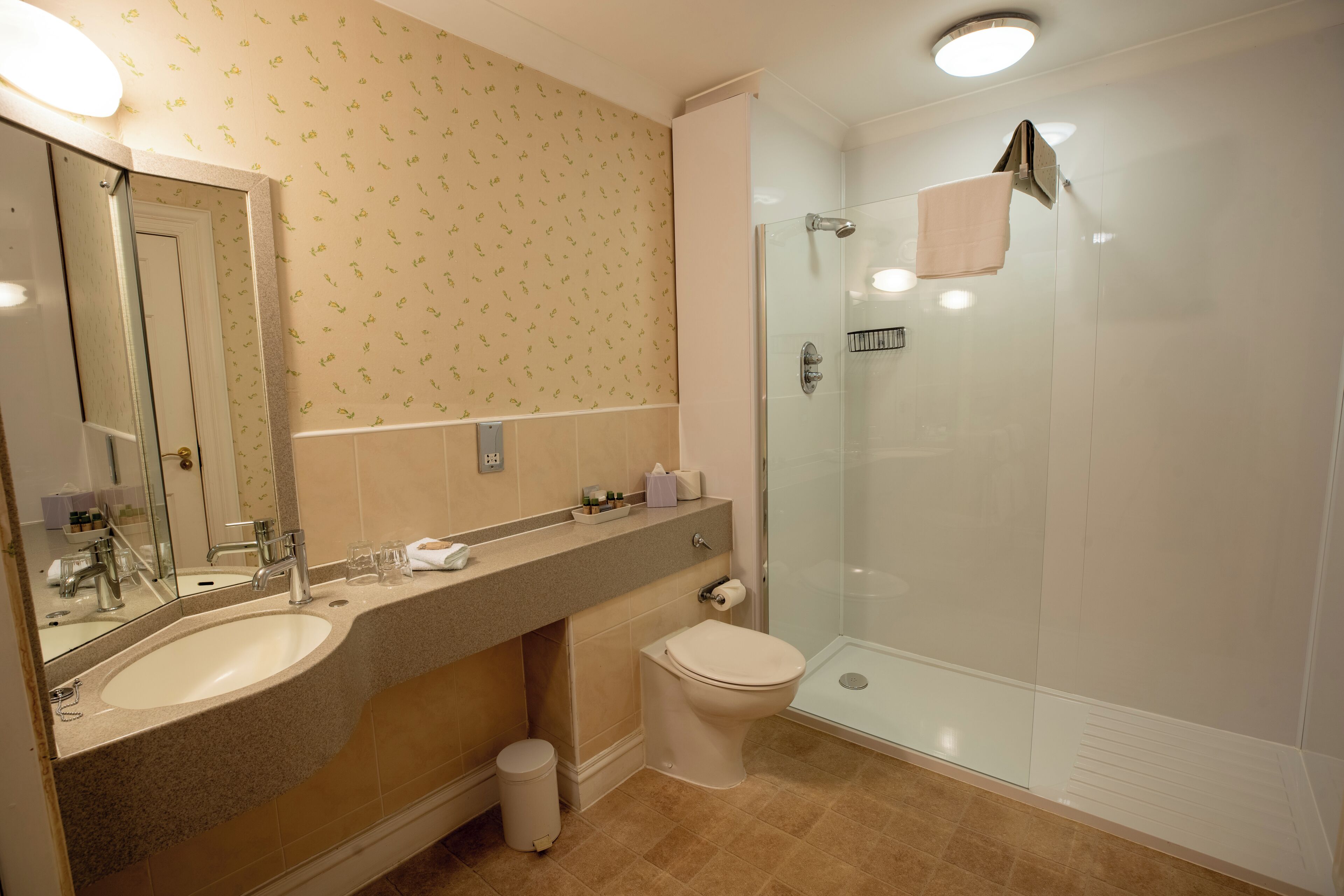 A bathroom with a sink, mirror, toilet, and glass-enclosed shower.