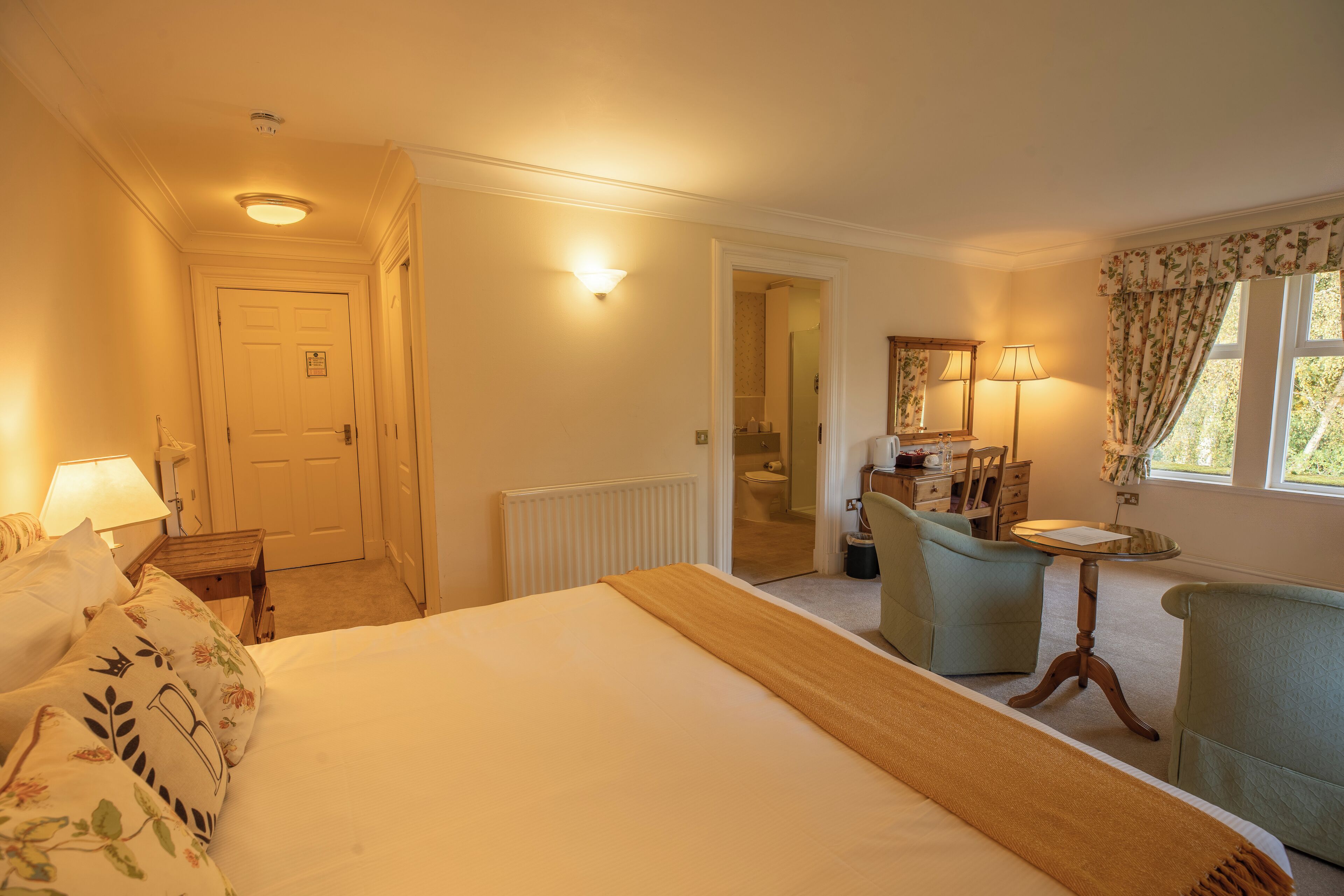 A hotel room with a bed, a desk, a chair, a lamp, and a window with curtains.