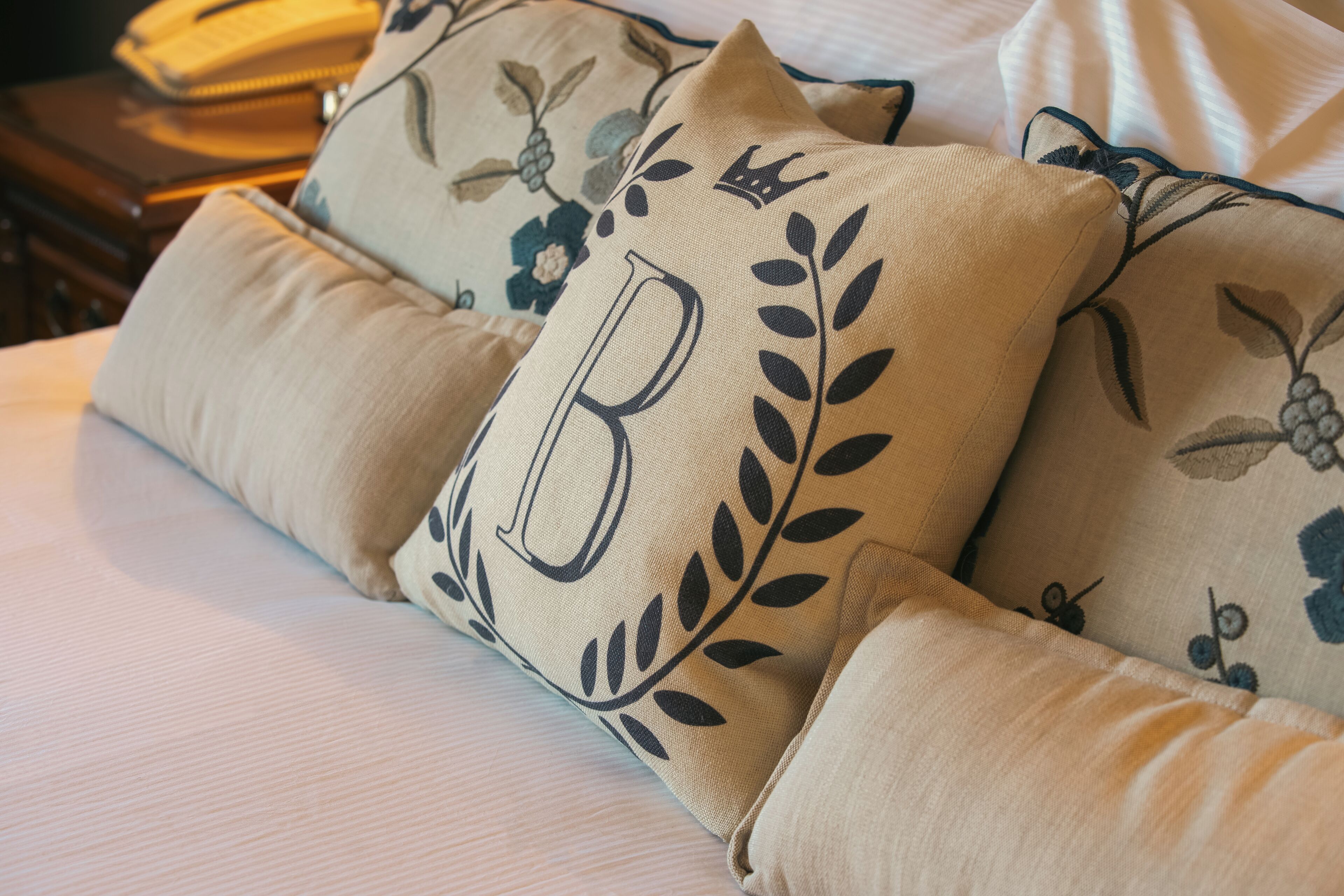 A bed with beige pillows featuring a large letter 'B' and floral patterns.