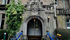 A historic building with a flag, stone architecture, and two bicycles parked in front. - Ballathie House Hotel (Perth)