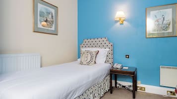 Un dormitorio con cama, una mesita de noche con lámpara y dos cuadros enmarcados en la pared.