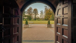 A view through a large wooden door archway into a paved courtyard with a bench and two planters. - Ballathie House Hotel (Perth)