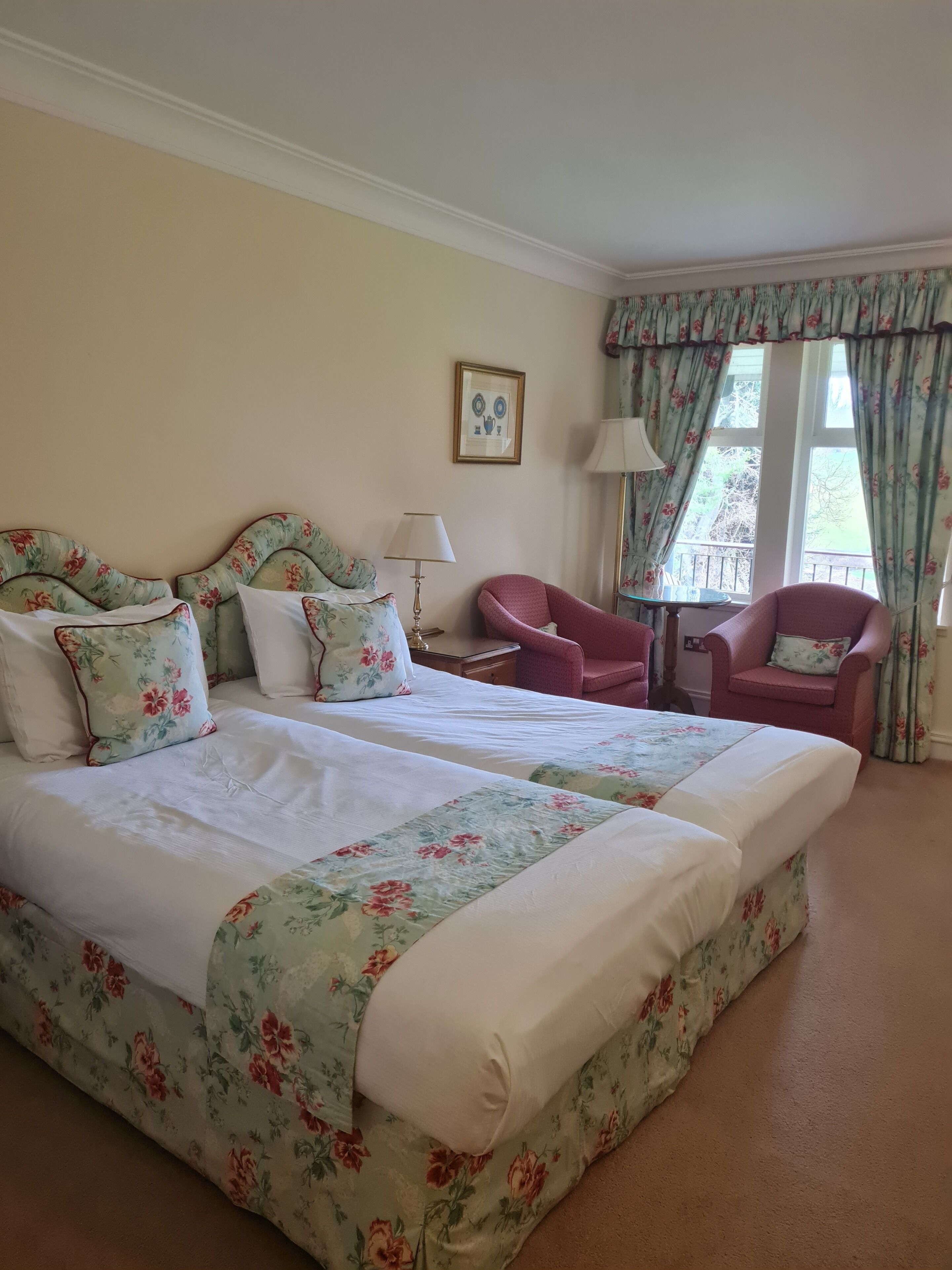 A hotel room with two beds, a chair, a table, and a window with curtains.