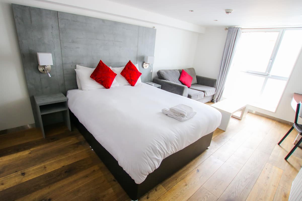 A modern hotel room with a large bed, grey headboard, and a grey sofa.