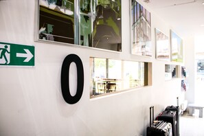 A wall with a green emergency exit sign, a large black letter 'O', and a window reflecting a dining area. - Brunswick Merchant City Hotel (Glasgow)