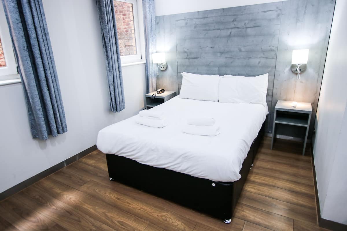 A modern hotel room with a large bed, wooden flooring, and two bedside tables with lamps.