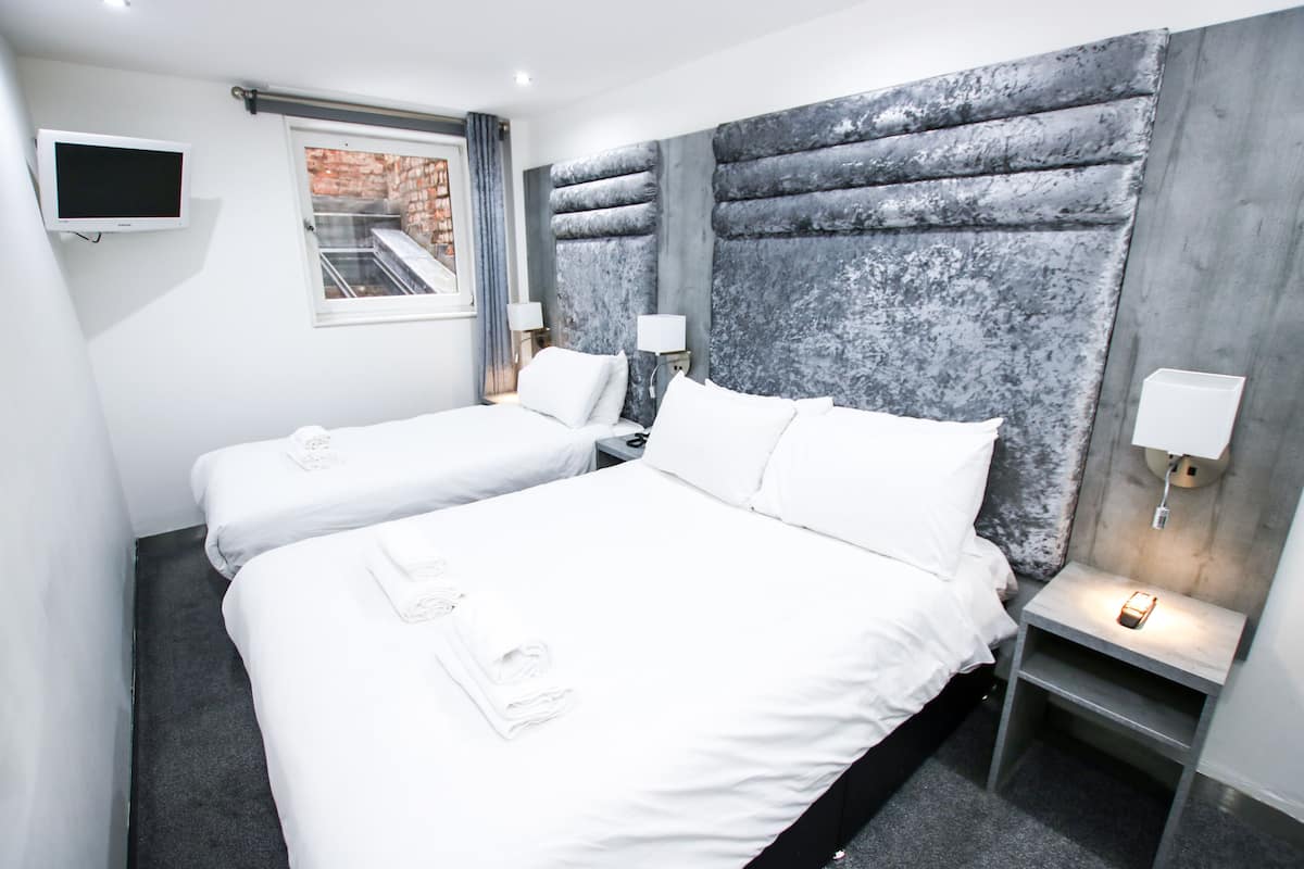 A hotel room with two beds, a TV, a window with a view, and a modern headboard.