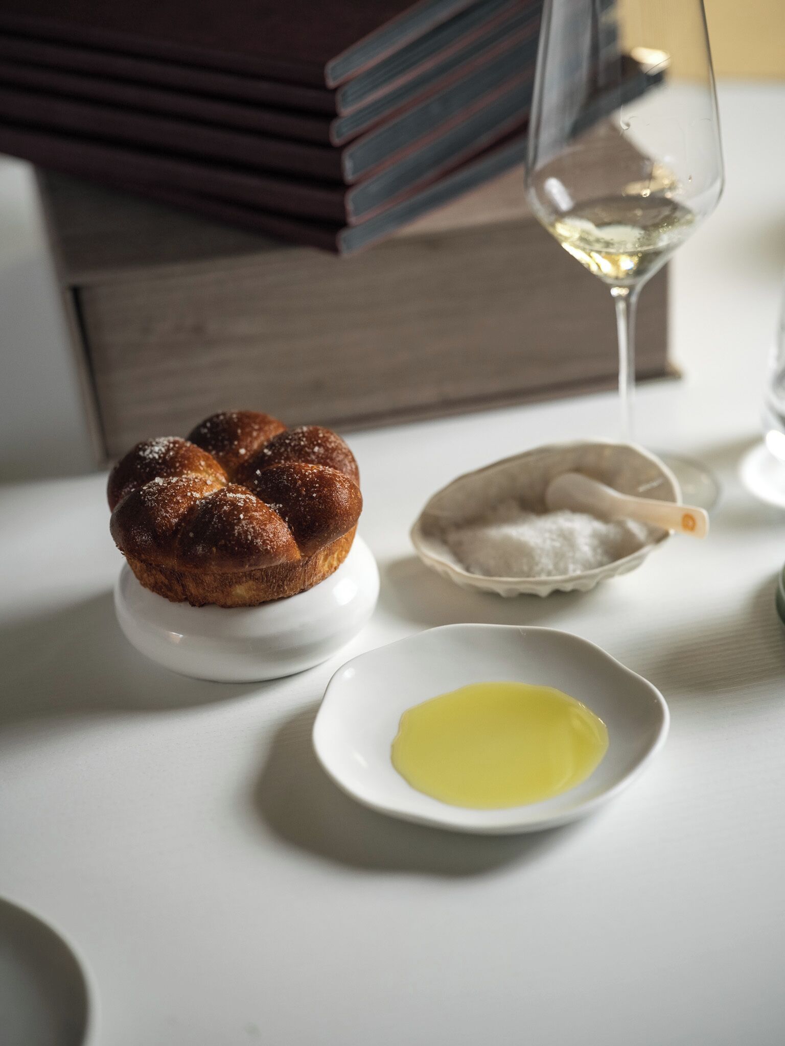 A dessert on a white plate, a small bowl of sugar, and a glass of white wine on a table.