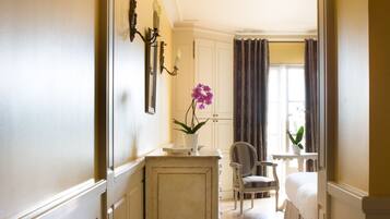 A hallway with a bed, a chair, and a small table with a vase of flowers.