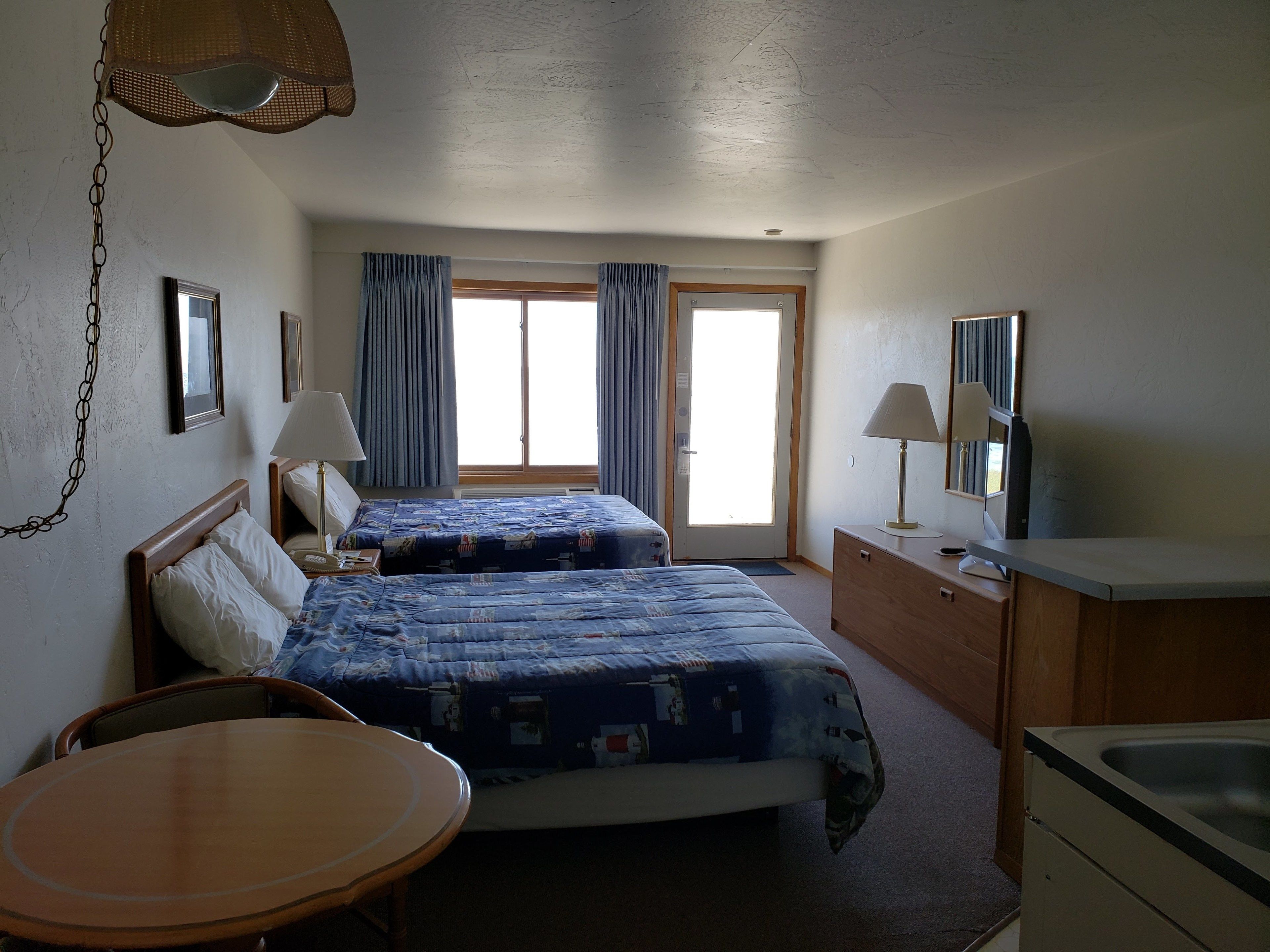 Ett hotellrum med två sängar, en trästol, ett litet bord, ett skrivbord med en lampa och ett handfat.