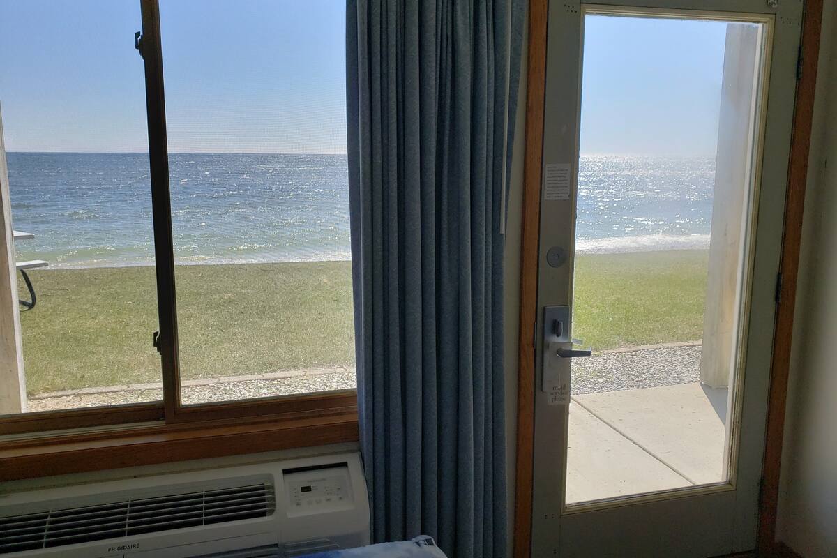 Una habitación con vista al mar a través de una ventana, una puerta y un equipo de aire acondicionado instalado en la pared.