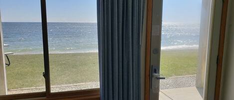 A room with a view of the sea through a window, a door, and a wall-mounted air conditioning unit.