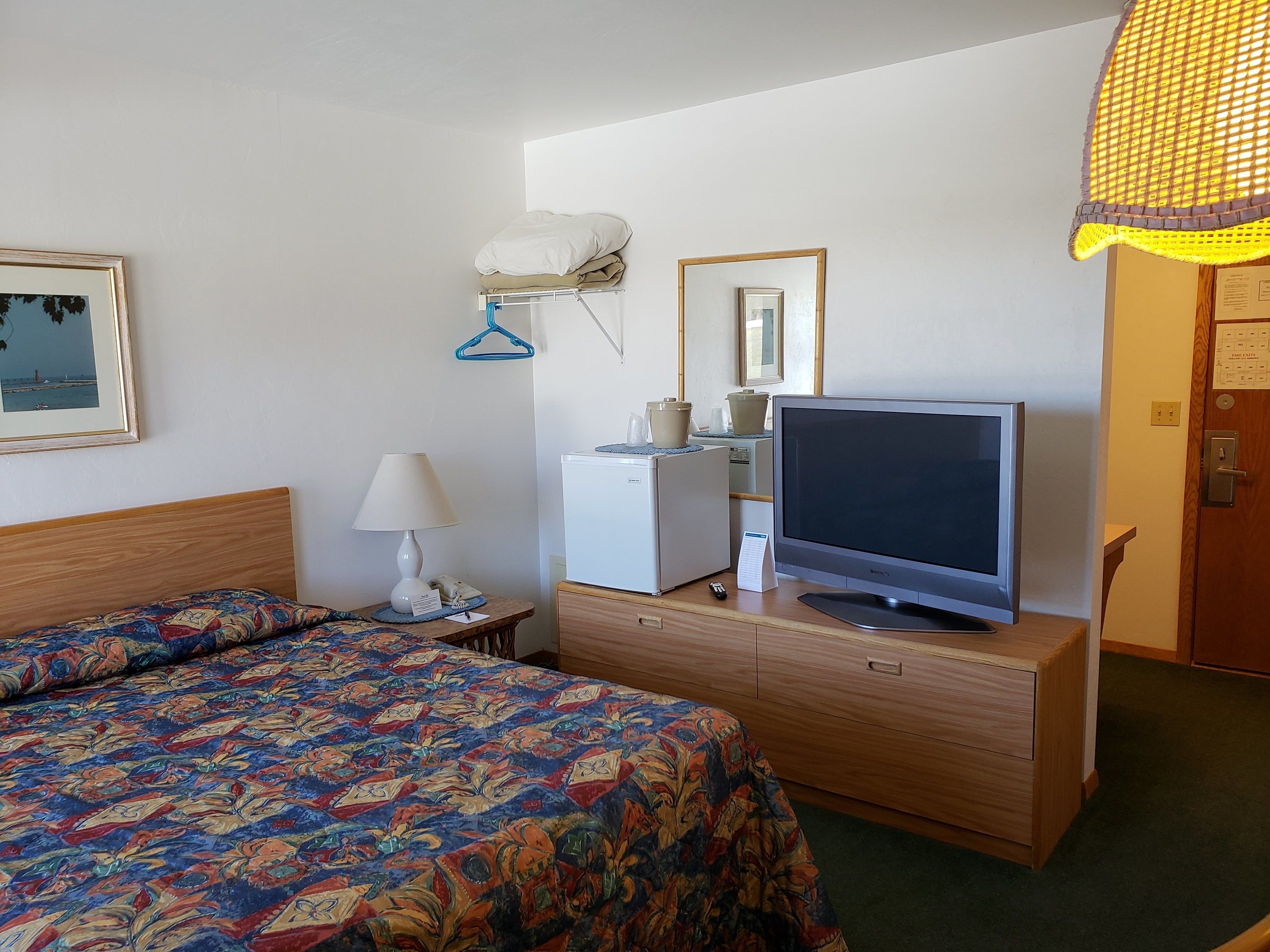 A hotel room with a bed, a desk with a computer, a television, and a small refrigerator.