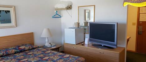 Habitación de hotel con cama, escritorio, computadora, televisor y refrigerador pequeño.