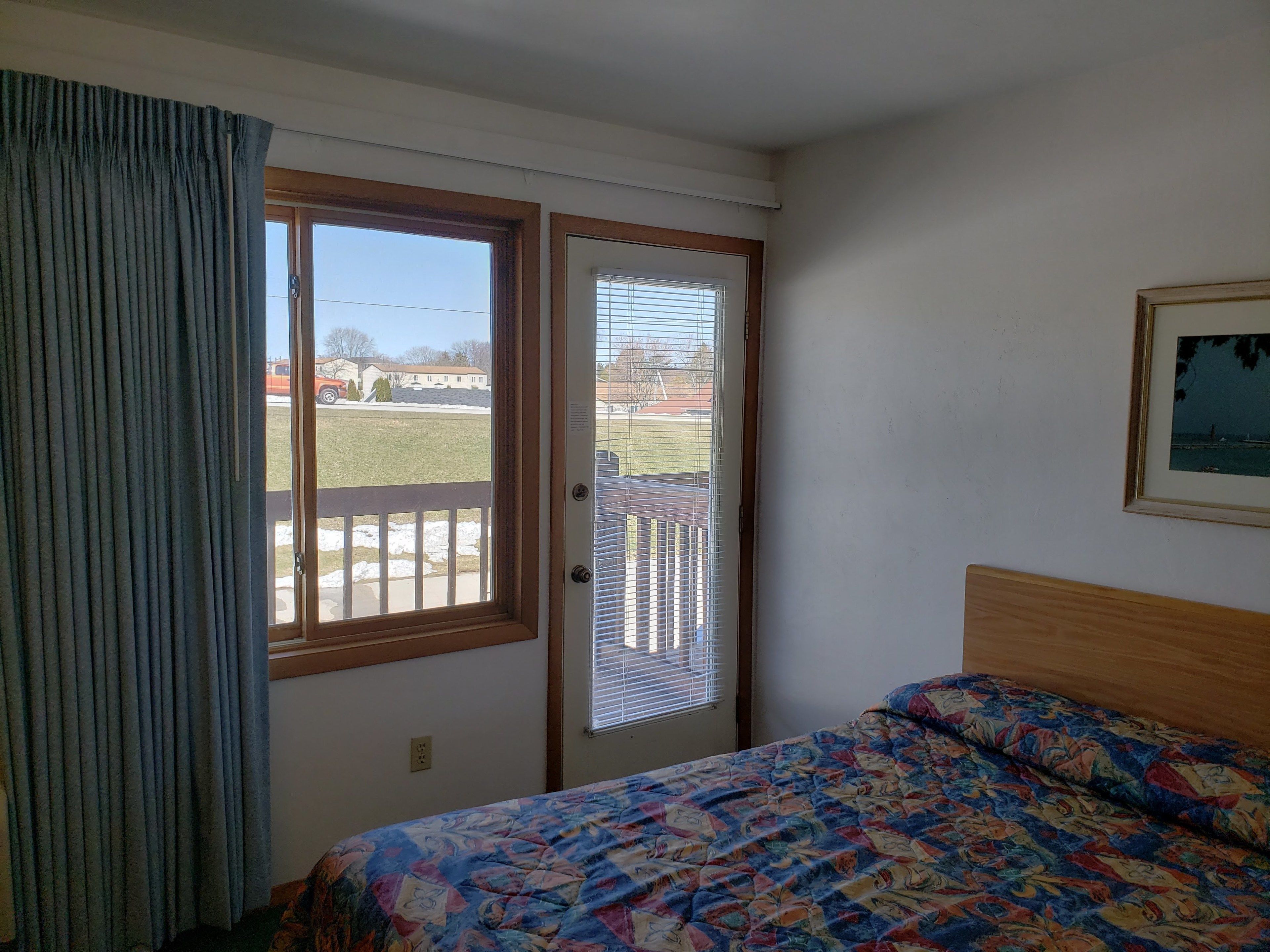 A bedroom with a bed, a door with a view to the outside, and a framed picture on the wall.